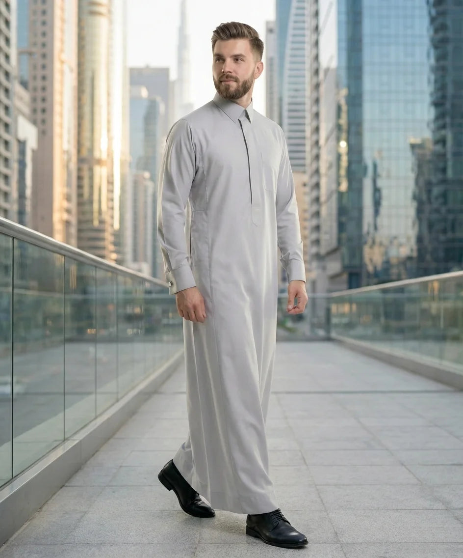 Light Grey Luxury Thobe styled in a contemporary urban business environment, highlighting premium craftsmanship, exceptional comfort, executive elegance, and modern Gulf fashion for professionals seeking confidence, sophistication, prestige, and timeless style. ثوب رمادي فاتح فاخر بإطلالة عصرية في بيئة أعمال راقية يجمع بين الفخامة الخليجية والأناقة الحديثة للمناسبات الرسمية والعملية.