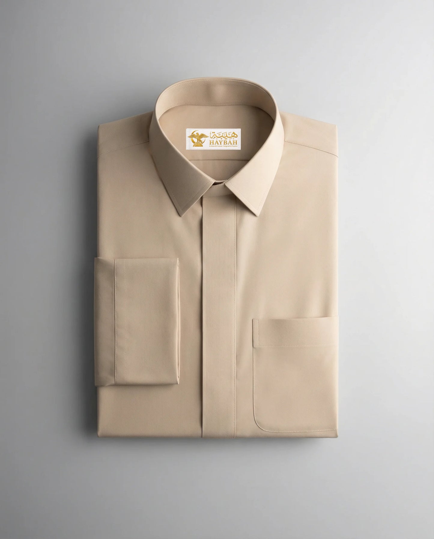 Folded Desert Beige Executive Thobe showcasing premium craftsmanship, luxurious beige fabric, concealed placket, refined stitching, structured collar, and sophisticated Gulf-inspired tailoring by Haybah for elegant formal wear and distinguished occasions. ثوب بيج فاخر مطوي بعناية يبرز جودة الخياطة الراقية والتفاصيل الدقيقة والتصميم العصري المناسب للمناسبات الرسمية.