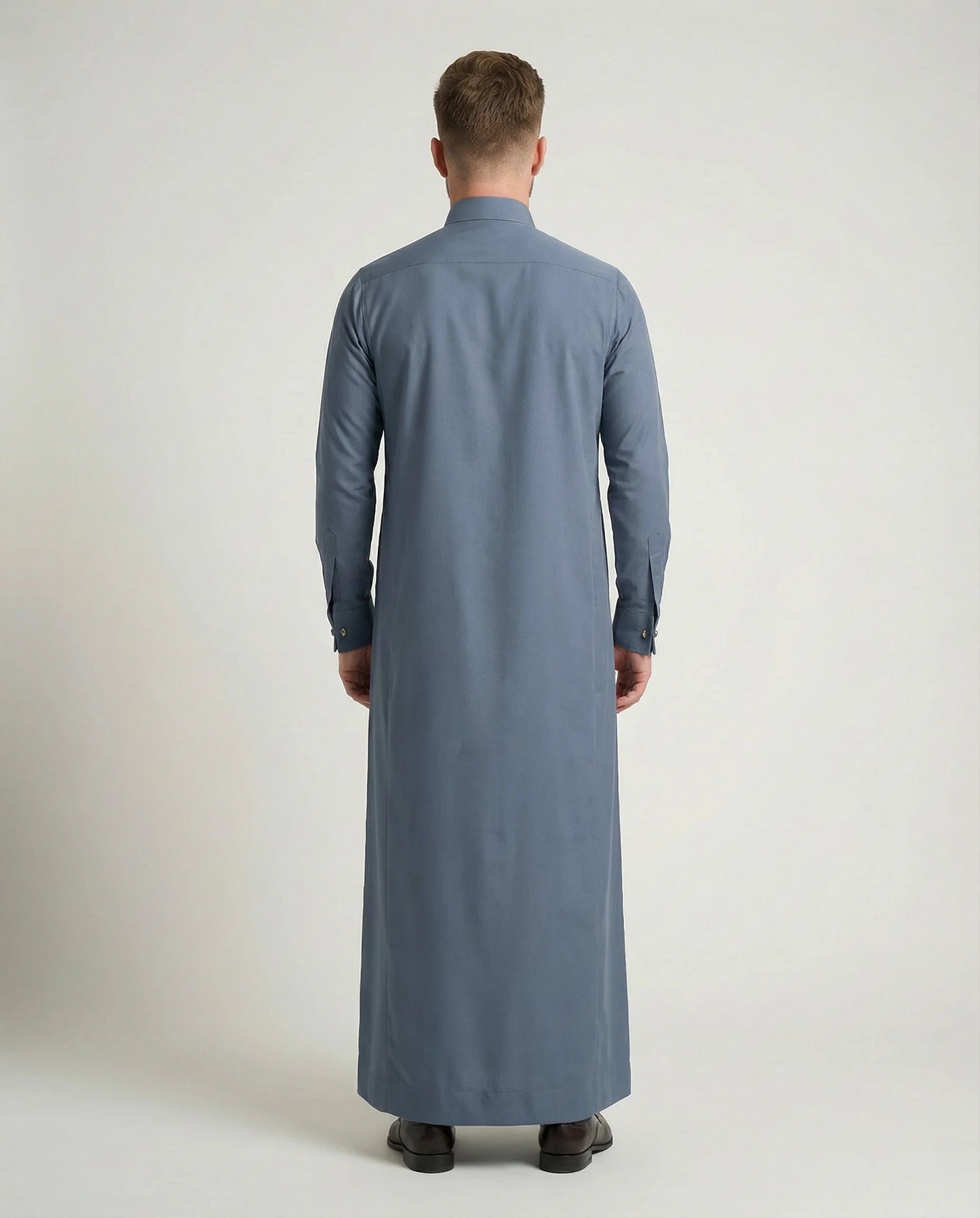 Side profile view of Formal Slate Blue Premium Thobe highlighting its clean silhouette, precise tailoring, concealed placket, structured collar, premium fabric drape, and refined professional appearance. منظر جانبي لثوب أزرق أردوازي فاخر يبرز القصة الأنيقة والانسيابية الراقية والتفاصيل الاحترافية المصممة للرجل العصري.