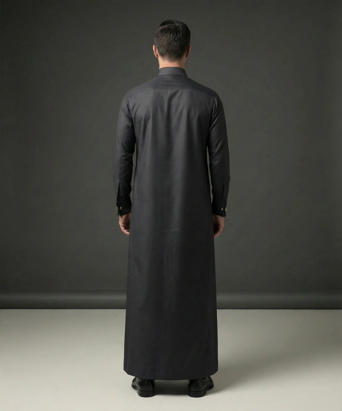 Back view of Smoke Black Executive Thobe highlighting clean tailoring, graceful drape, premium construction, elegant silhouette, and timeless Gulf formalwear styling suitable for weddings, Eid gatherings, nikah ceremonies, luxury occasions, and executive wear. منظر خلفي لثوب أسود دخاني فاخر يظهر الانسيابية الراقية والتفصيل الاحترافي والمظهر الأنيق المناسب للمناسبات المميزة.