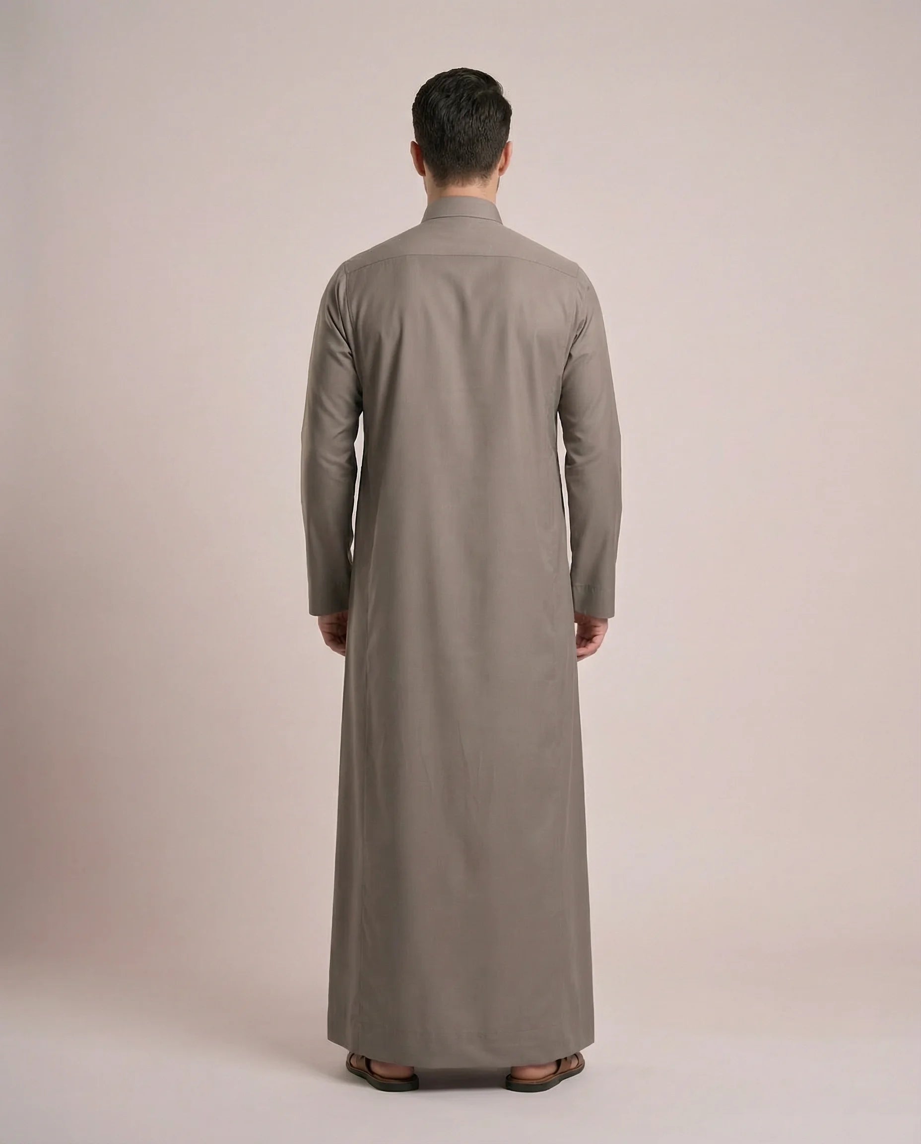 Back view of Warm Grey Everyday Thobe Contemporary Classic showcasing clean tailoring, full-length modest silhouette, balanced proportions, and premium fabric drape. Men's Saudi thobe, luxury Arabic clothing, premium jubba, ثوب رجالي سعودي, ثوب رسمي رجالي, جلابية رجالية طويلة, ملابس إسلامية رجالية فاخرة, modern Islamic fashion combining traditional elegance, comfort, professionalism, and timeless Middle Eastern style.