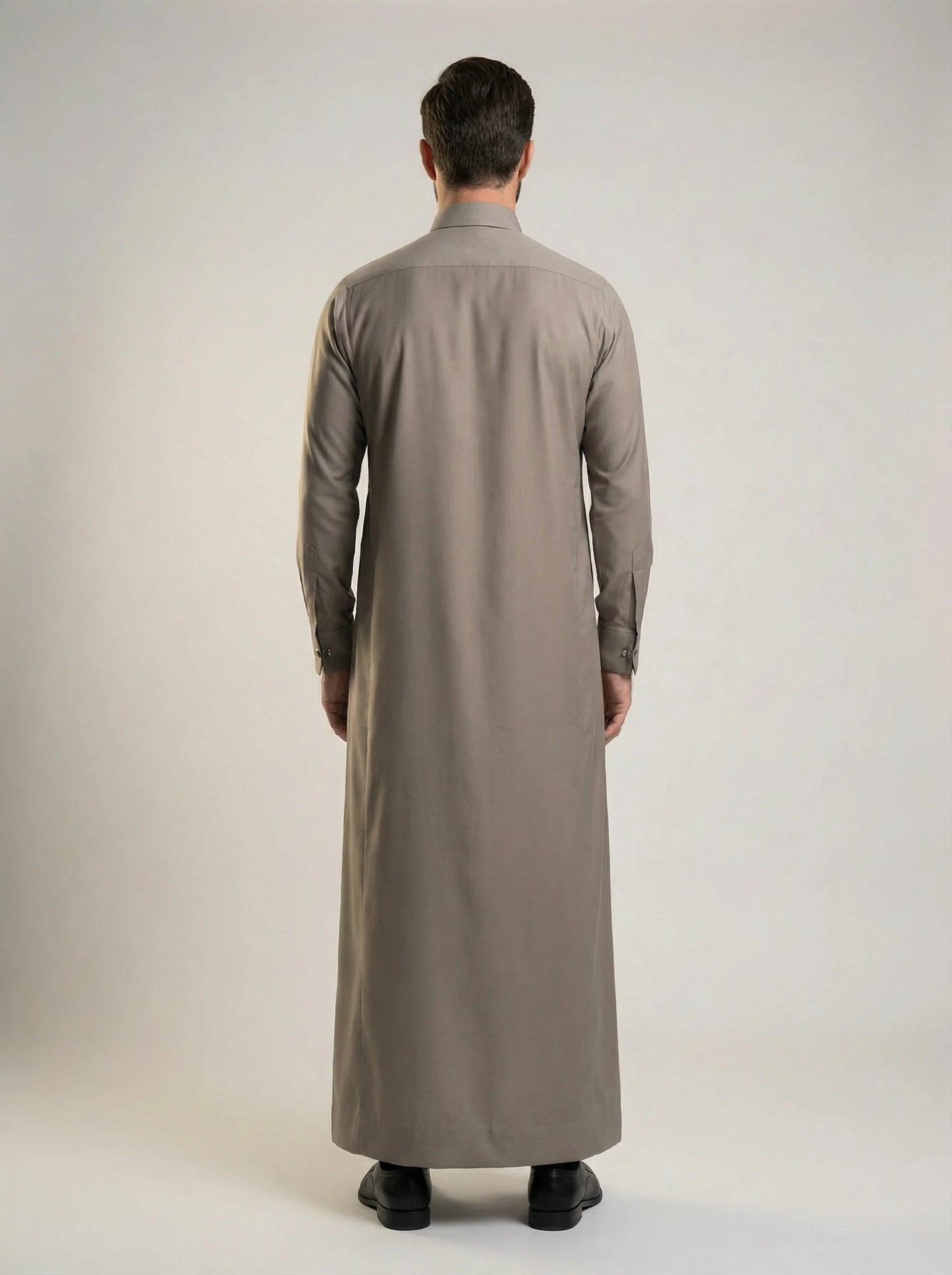 Back view of Warm Grey Luxury Thobe highlighting its clean tailored construction, graceful fabric drape, balanced silhouette, premium craftsmanship, and elegant ceremonial styling crafted for weddings, formal occasions, and refined Gulf fashion. منظر خلفي لثوب رمادي دافئ فاخر يظهر القصة المتوازنة والانسيابية الأنيقة والتفصيل الاحترافي المناسب للمناسبات الراقية والاحتفالات الرسمية.