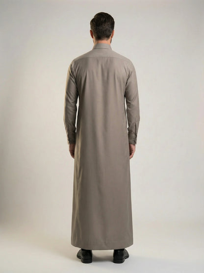 Back view of Warm Grey Luxury Thobe highlighting its clean tailored construction, graceful fabric drape, balanced silhouette, premium craftsmanship, and elegant ceremonial styling crafted for weddings, formal occasions, and refined Gulf fashion. منظر خلفي لثوب رمادي دافئ فاخر يظهر القصة المتوازنة والانسيابية الأنيقة والتفصيل الاحترافي المناسب للمناسبات الراقية والاحتفالات الرسمية.