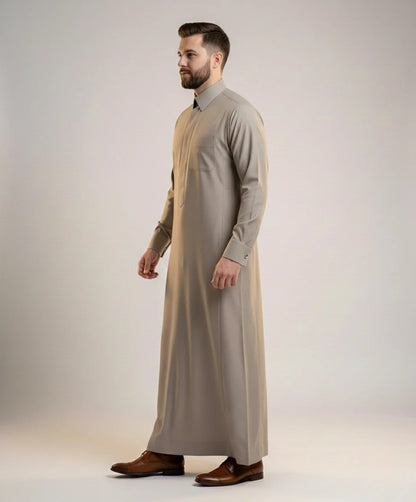 Side profile of Executive Sand Grey Thobe featuring a streamlined silhouette, concealed placket, structured collar, luxury tailoring, premium comfort, and timeless Gulf elegance crafted for formal gatherings, weddings, corporate events, and executive wear. منظر جانبي لثوب رمادي رملي فاخر يبرز القصة الأنيقة والتفاصيل الدقيقة والفخامة الخليجية الراقية.