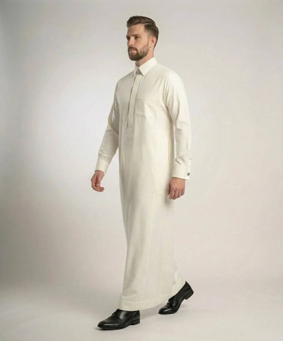 Side walking view of Off-White Royal Executive Thobe featuring luxury tailoring, structured fit, premium off-white fabric, concealed placket, and modern executive elegance. منظر جانبي أثناء الحركة لثوب أوف وايت فاخر يبرز التصميم العصري والقصة الأنيقة والخياطة الدقيقة التي تعكس الفخامة والرقي.