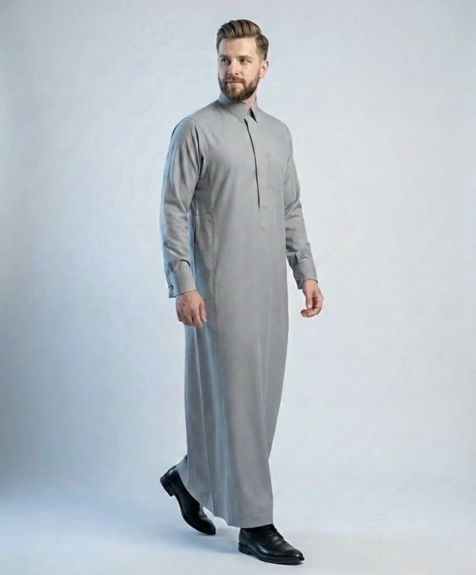 Walking view of Stone Grey Signature Thobe featuring timeless elegance, breathable premium fabric, concealed placket, executive tailoring, and refined formal styling designed for confident professional wear and distinguished occasions. إطلالة أثناء المشي لثوب رمادي حجري فاخر تبرز الأناقة العصرية والراحة العالية والخياطة المتقنة للرجل الأنيق.