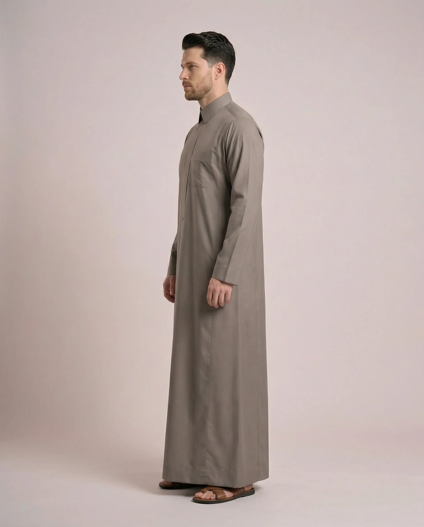 Side profile of Warm Grey Everyday Saudi Thobe highlighting streamlined tailoring, structured turn-down collar, clean silhouette, and sophisticated warm grey tone. Luxury men's thobe, Saudi jubba, Arabic clothing, ثوب سعودي أنيق, ثوب رجالي فاخر, دشداشة رجالية رسمية, جلابية رجالية مودرن, premium modest wear crafted for office professionals, family gatherings, Eid events, Ramadan evenings, and distinguished everyday elegance.