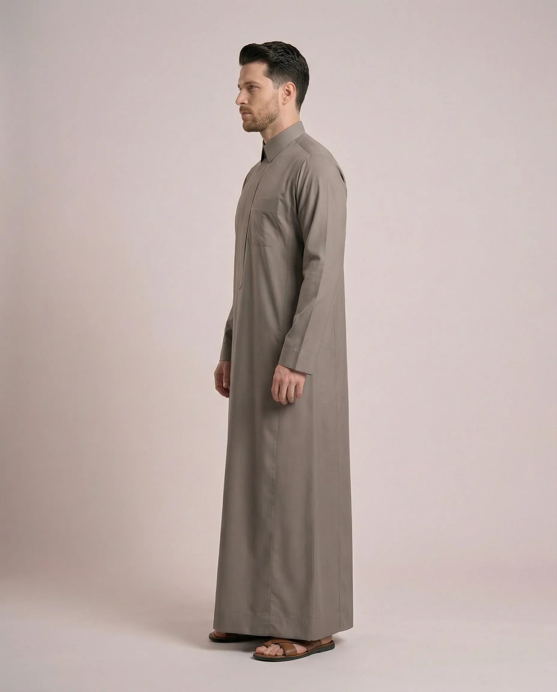 Side profile of Warm Grey Everyday Saudi Thobe highlighting streamlined tailoring, structured turn-down collar, clean silhouette, and sophisticated warm grey tone. Luxury men's thobe, Saudi jubba, Arabic clothing, ثوب سعودي أنيق, ثوب رجالي فاخر, دشداشة رجالية رسمية, جلابية رجالية مودرن, premium modest wear crafted for office professionals, family gatherings, Eid events, Ramadan evenings, and distinguished everyday elegance.