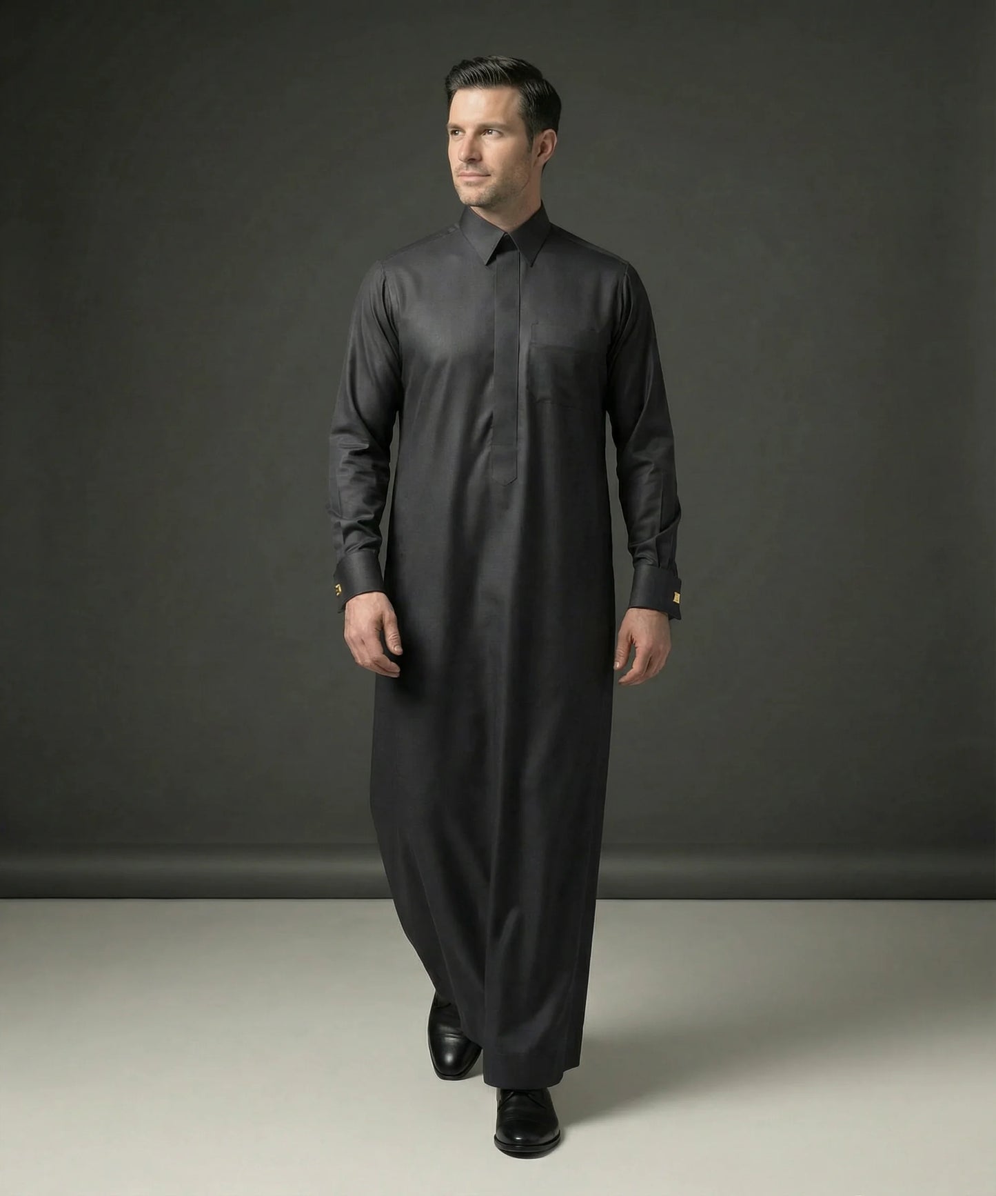 Front walking view of Smoke Black Executive Thobe displaying elegant tailoring, premium fabric, concealed placket design, executive sophistication, and refined Gulf style ideal for weddings, formal gatherings, business occasions, Eid celebrations, and luxury menswear collections. إطلالة أمامية لثوب أسود دخاني فاخر تعكس الرقي والأناقة والفخامة المناسبة للمناسبات الرسمية والاحتفالات الراقية.
