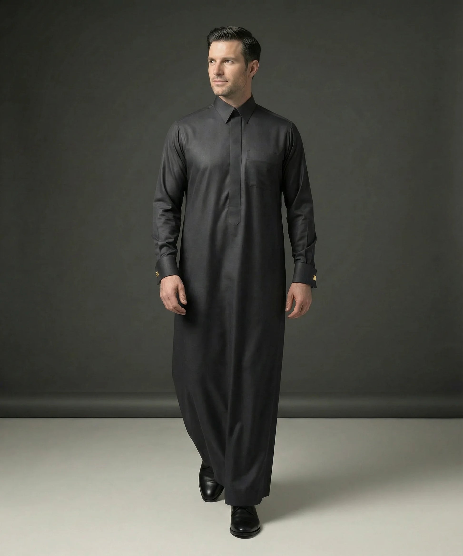 Front walking view of Smoke Black Executive Thobe displaying elegant tailoring, premium fabric, concealed placket design, executive sophistication, and refined Gulf style ideal for weddings, formal gatherings, business occasions, Eid celebrations, and luxury menswear collections. إطلالة أمامية لثوب أسود دخاني فاخر تعكس الرقي والأناقة والفخامة المناسبة للمناسبات الرسمية والاحتفالات الراقية.