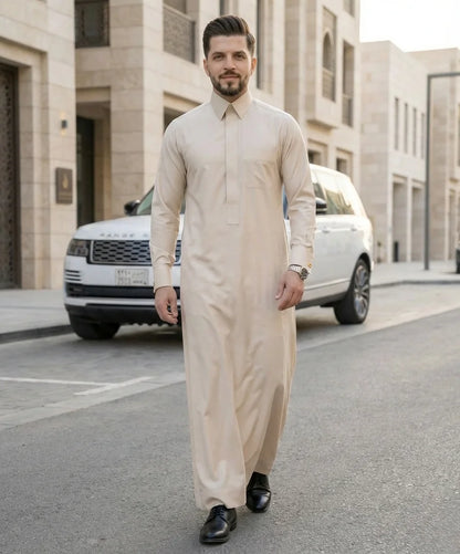 Pearl Beige Modern Formal Thobe styled in an upscale urban Gulf setting, combining luxury craftsmanship, contemporary elegance, premium comfort, and refined professional style for modern gentlemen. ثوب بيج لؤلؤي فاخر بإطلالة مستوحاة من أسلوب الحياة الخليجية الراقية يجمع بين الفخامة العصرية والراحة والأناقة الكلاسيكية للرجل المتميز.