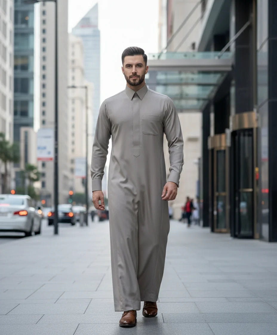 Luxury Sand Grey Executive Thobe by Haybah styled in a modern business district setting, highlighting premium craftsmanship, breathable comfort, executive sophistication, and timeless formal fashion for contemporary gentlemen. ثوب رمادي رملي فاخر بإطلالة عصرية في بيئة أعمال راقية يجمع بين الفخامة والراحة والأناقة ليمنح الرجل حضوراً استثنائياً في الاجتماعات والمناسبات الرسمية.