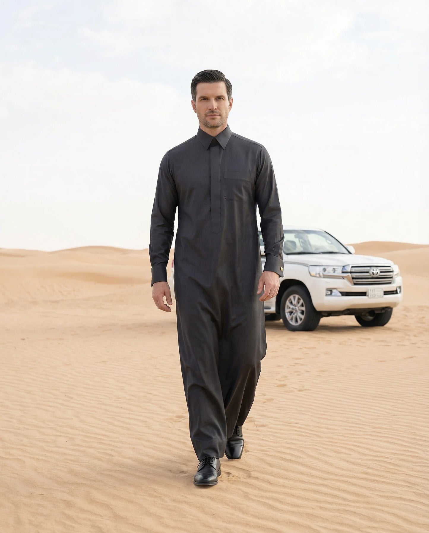 Smoke Black Executive Thobe styled in a luxury desert setting, showcasing premium craftsmanship, executive elegance, exceptional comfort, and contemporary Gulf fashion for gentlemen seeking prestige, confidence, and distinguished formal wear. ثوب أسود دخاني فاخر بإطلالة صحراوية راقية يجمع بين الأناقة الخليجية والفخامة الحديثة للمناسبات الرسمية والعملية.