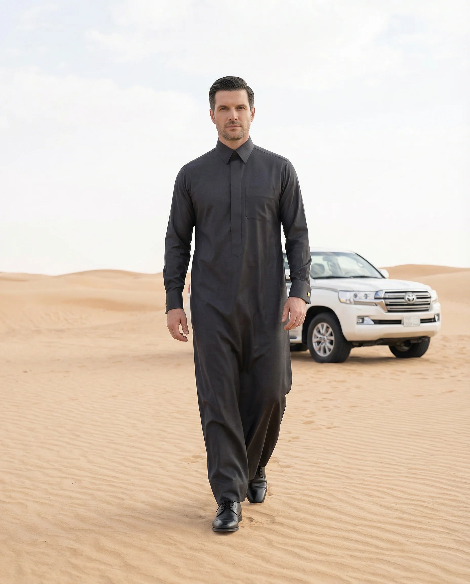 Smoke Black Executive Thobe styled in a luxury desert setting, showcasing premium craftsmanship, executive elegance, exceptional comfort, and contemporary Gulf fashion for gentlemen seeking prestige, confidence, and distinguished formal wear. ثوب أسود دخاني فاخر بإطلالة صحراوية راقية يجمع بين الأناقة الخليجية والفخامة الحديثة للمناسبات الرسمية والعملية.