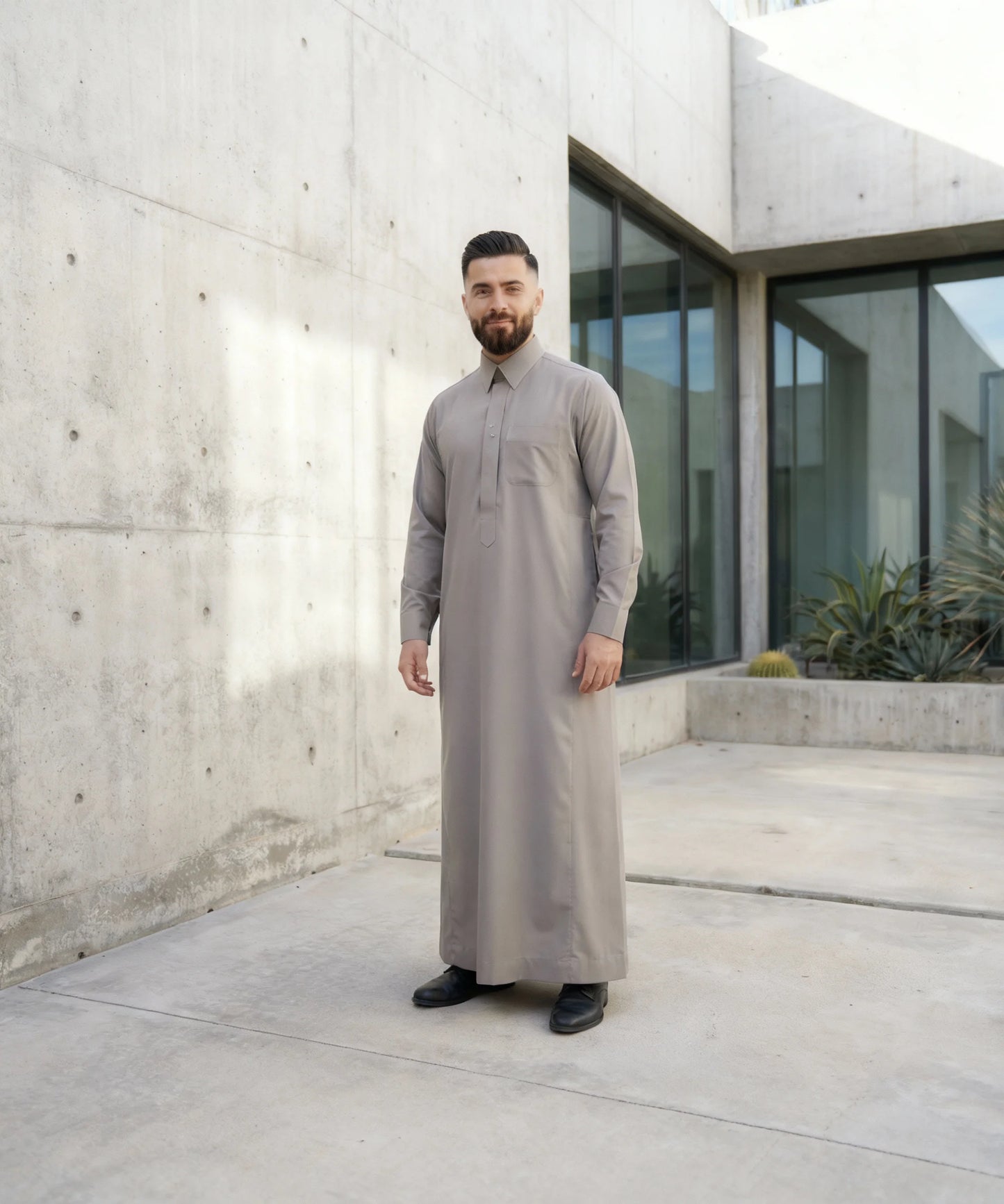 Urban Stone Grey Saudi Thobe worn in a contemporary architectural setting, showcasing modern Islamic fashion with understated luxury, clean tailoring, and versatile styling. Perfect for professionals seeking elegant modest wear that transitions seamlessly from formal occasions to everyday life.