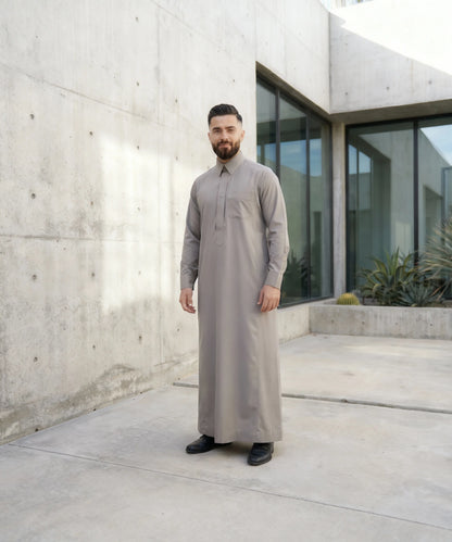 Urban Stone Grey Saudi Thobe worn in a contemporary architectural setting, showcasing modern Islamic fashion with understated luxury, clean tailoring, and versatile styling. Perfect for professionals seeking elegant modest wear that transitions seamlessly from formal occasions to everyday life.